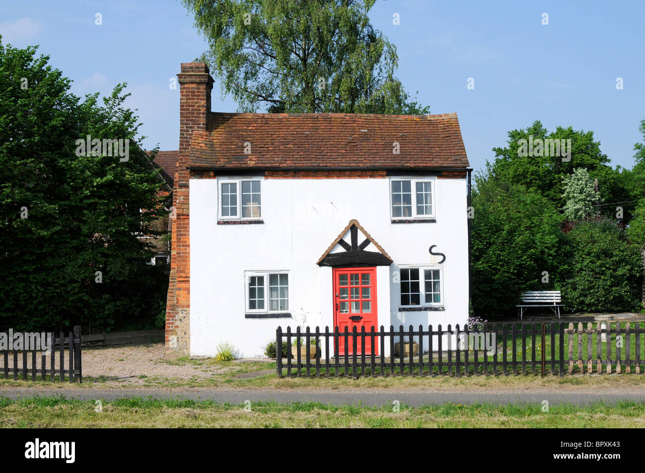A white tiled English country cottage with red door and garden seen from the front. Stock Photo