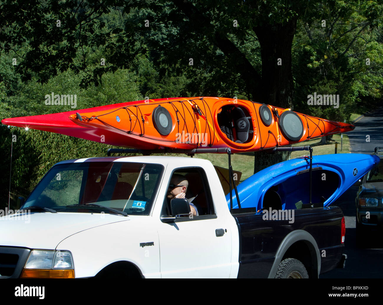 A pickup truck lorry loaded with orange and blue kayaks waiting in line to get to the boat launching area the boat ramp. Stock Photo