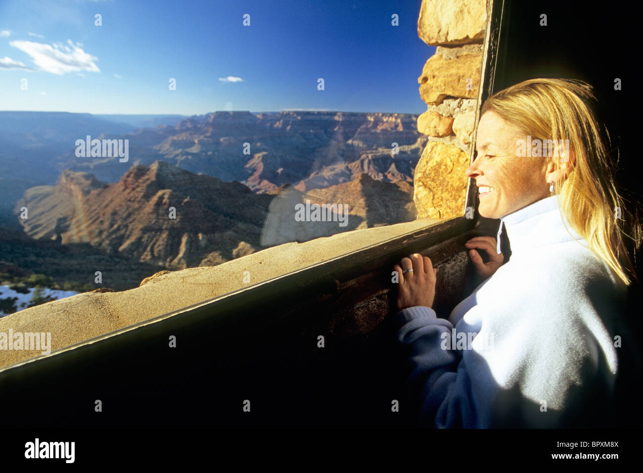 A woman looks through a window of a stone tower into the Grand Canyon ...