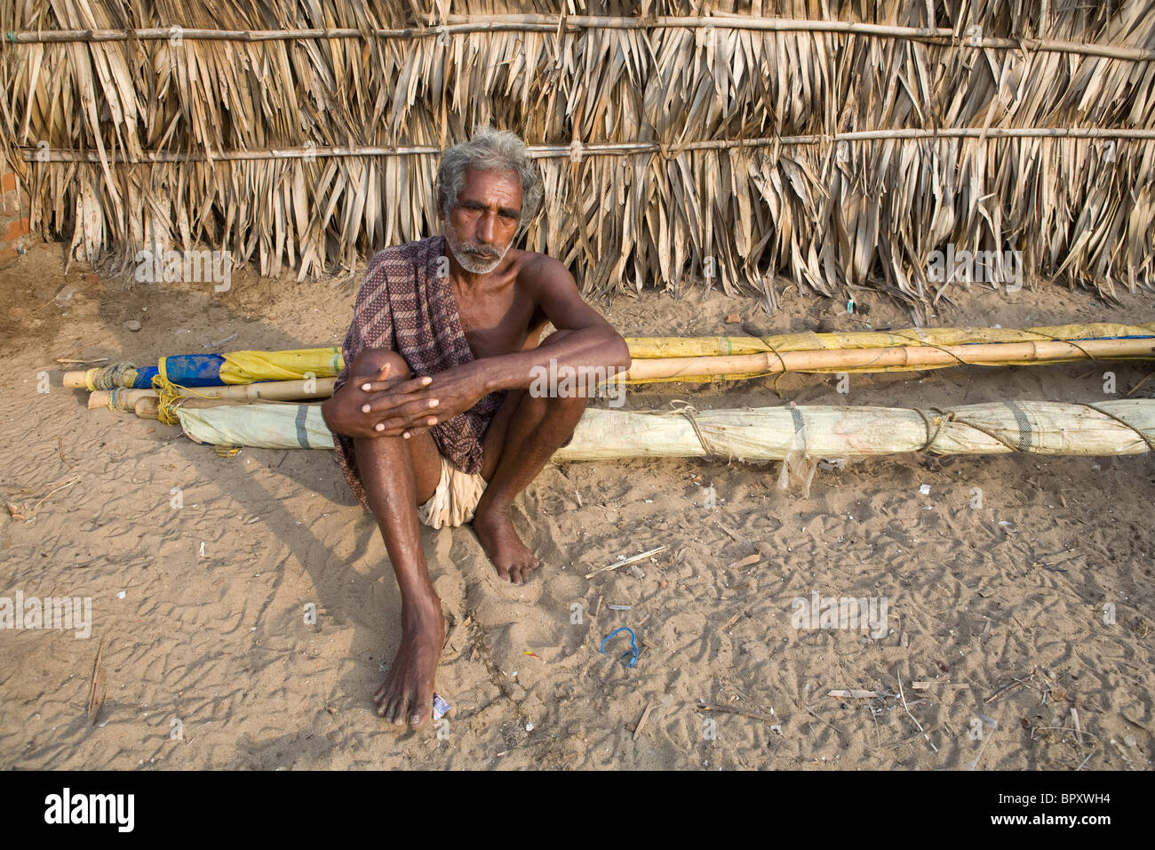 An old Indian fisherman seats behind a hut on the sand early in the morning at the fishing village in Puri, Orissa, India. Stock Photo