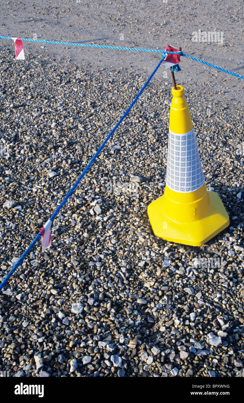 Yellow traffic cone with blue nylon ropes indicating no access or parking on area of gravel surface Stock Photo