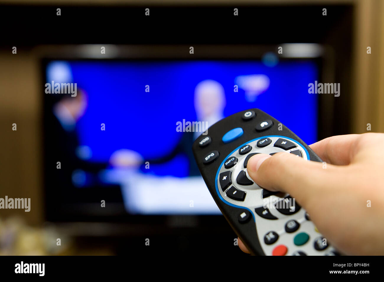 Hand holding TV remote control with a television in the background