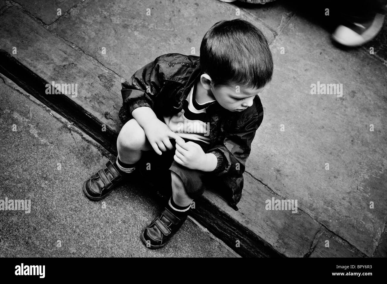 Boy sat on a curb in York looking down the street Stock Photo