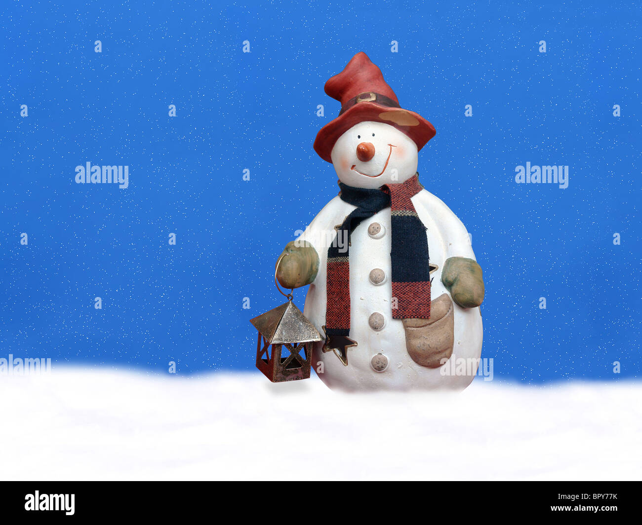 Snowman with red hat holding small lantern, reflecting in blue ice floe Stock Photo