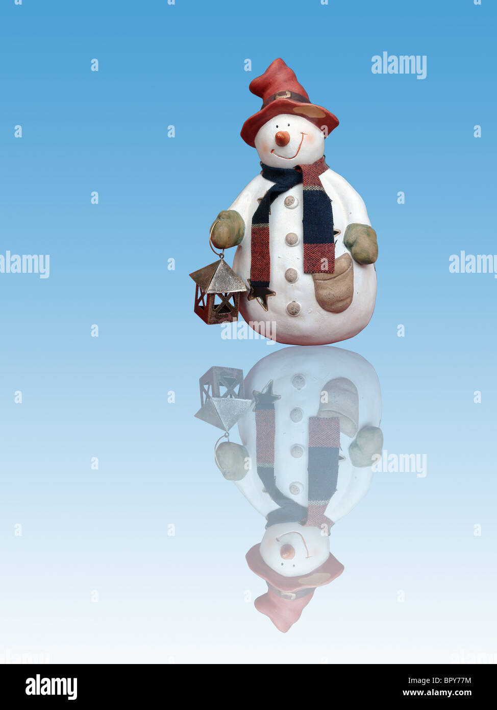 Snowman with red hat holding small lantern, reflecting in blue ice floe Stock Photo