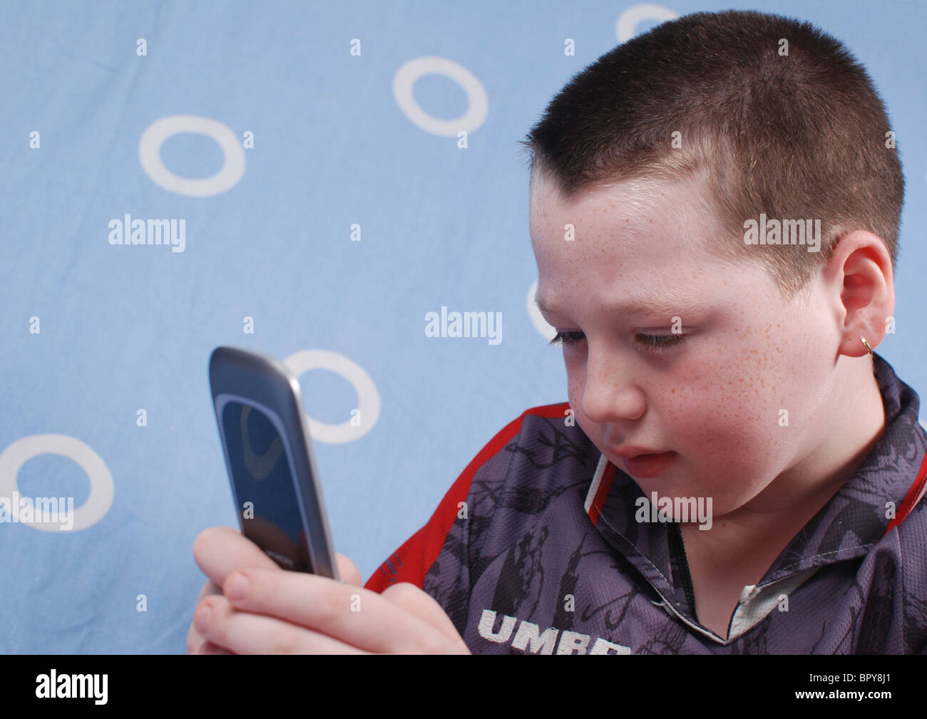 Boy of eight plays a game on his mobilr phone now a full entertainment centre. Model Release Available Stock Photo