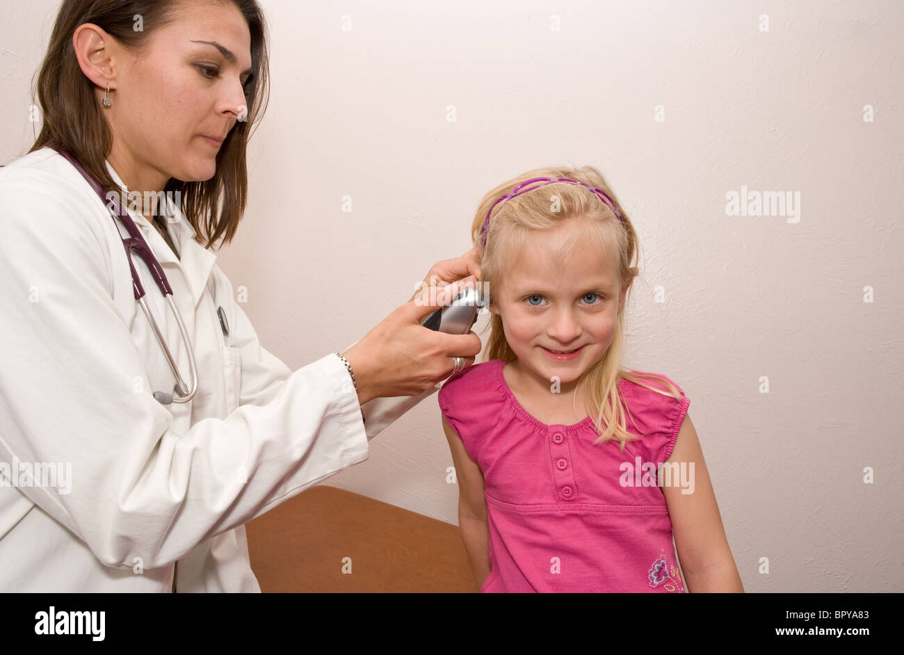 female physician takes child's temperature, in ear thermometer, checking for fever Stock Photo