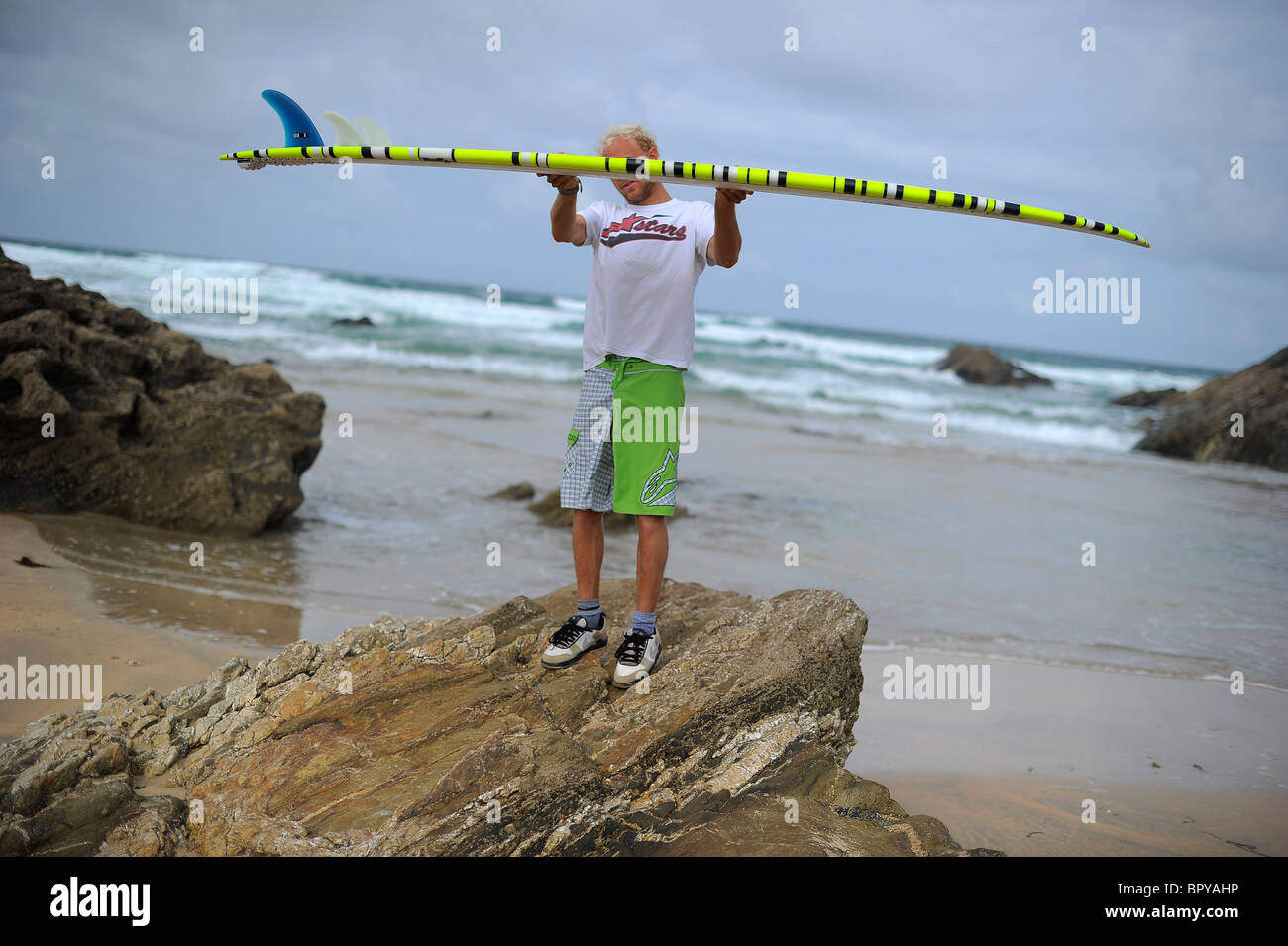 A surfer, Ben Howey, holding a longboard surfboard on the beach at