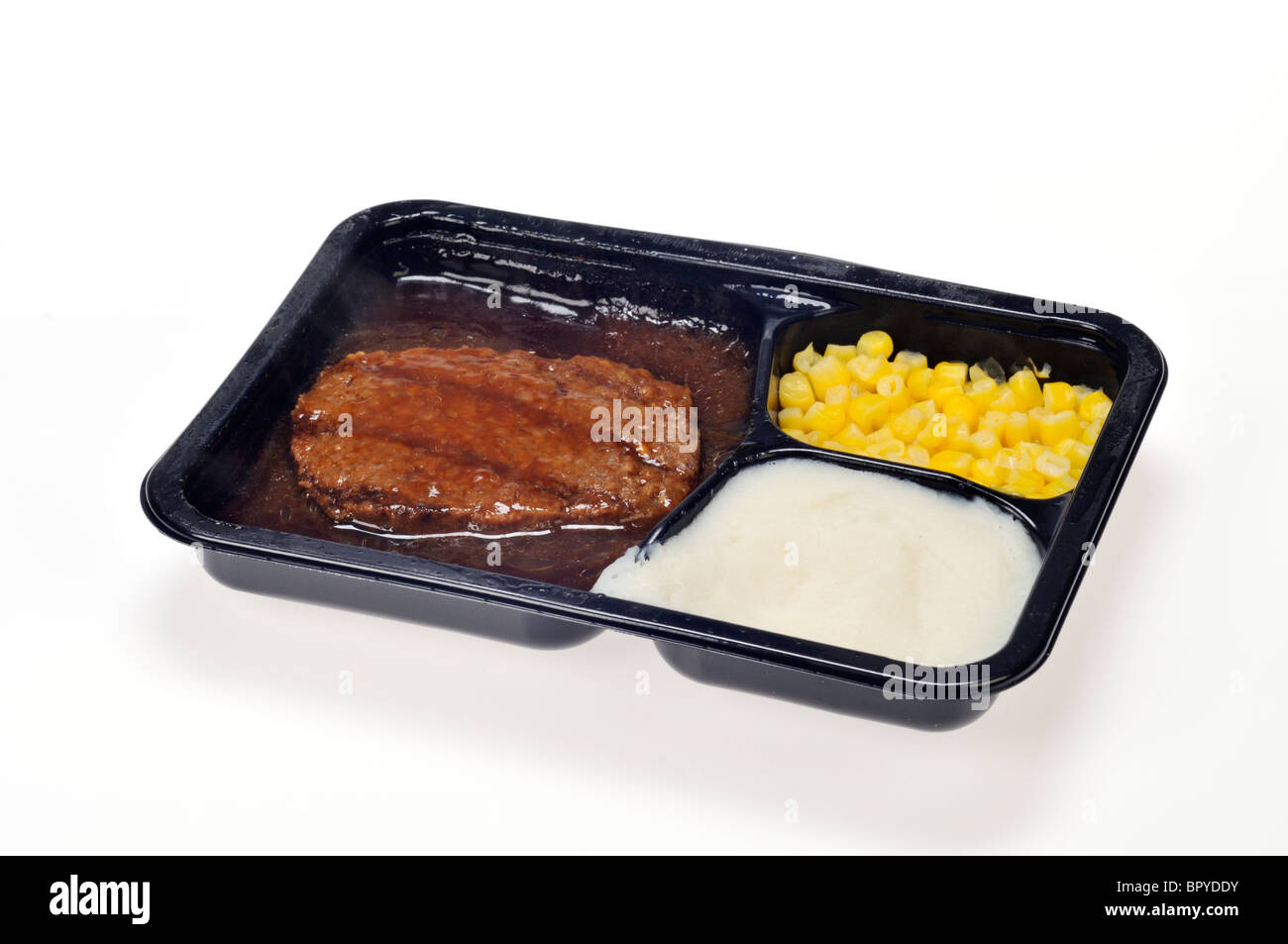 A cooked microwaved tv dinner, ready meal of salisbury steak, corn and mashed potatoes with gravy on white background, cutout. Stock Photo