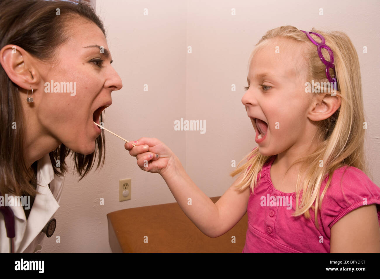 child looks into doctor's mouth with a tongue depressor, reversing