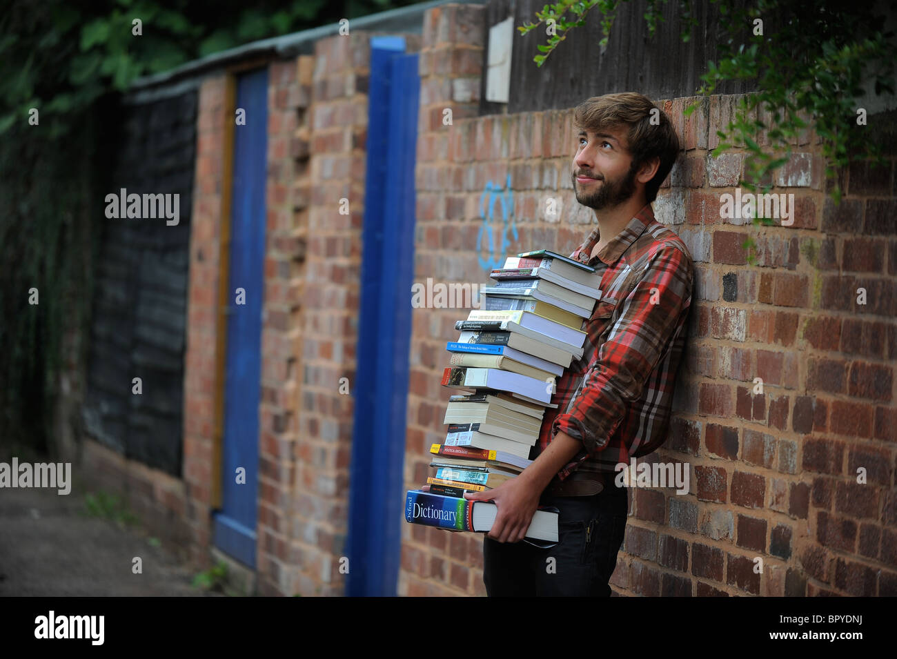 A student standing with a large pile of books, illustrating studying, revision, cramming and revising Stock Photo
