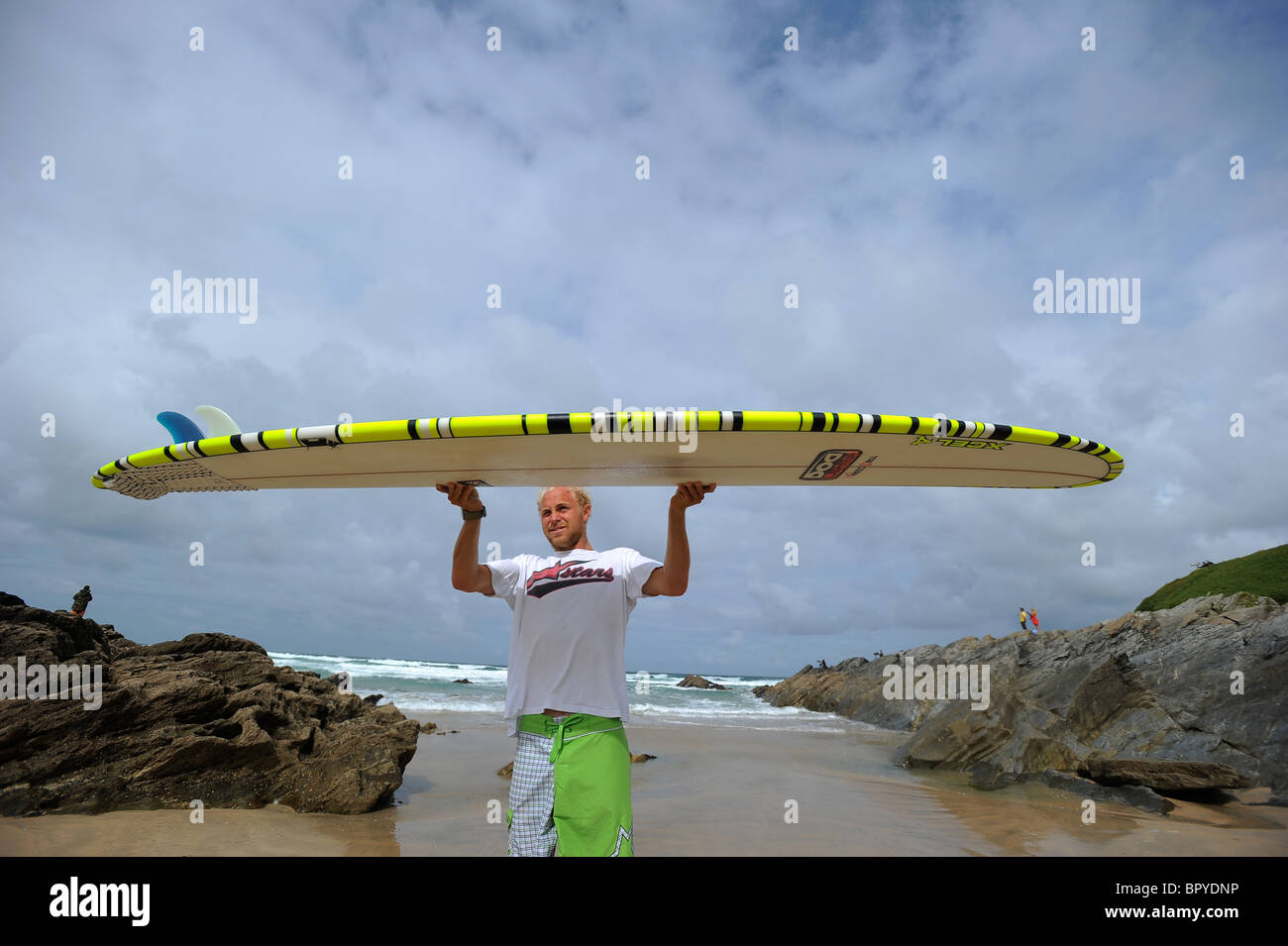 A surfer, Ben Howey, holding a longboard surfboard on the beach at Fistral, Newquay, the UK's surfing capital, in Cornwall Stock Photo