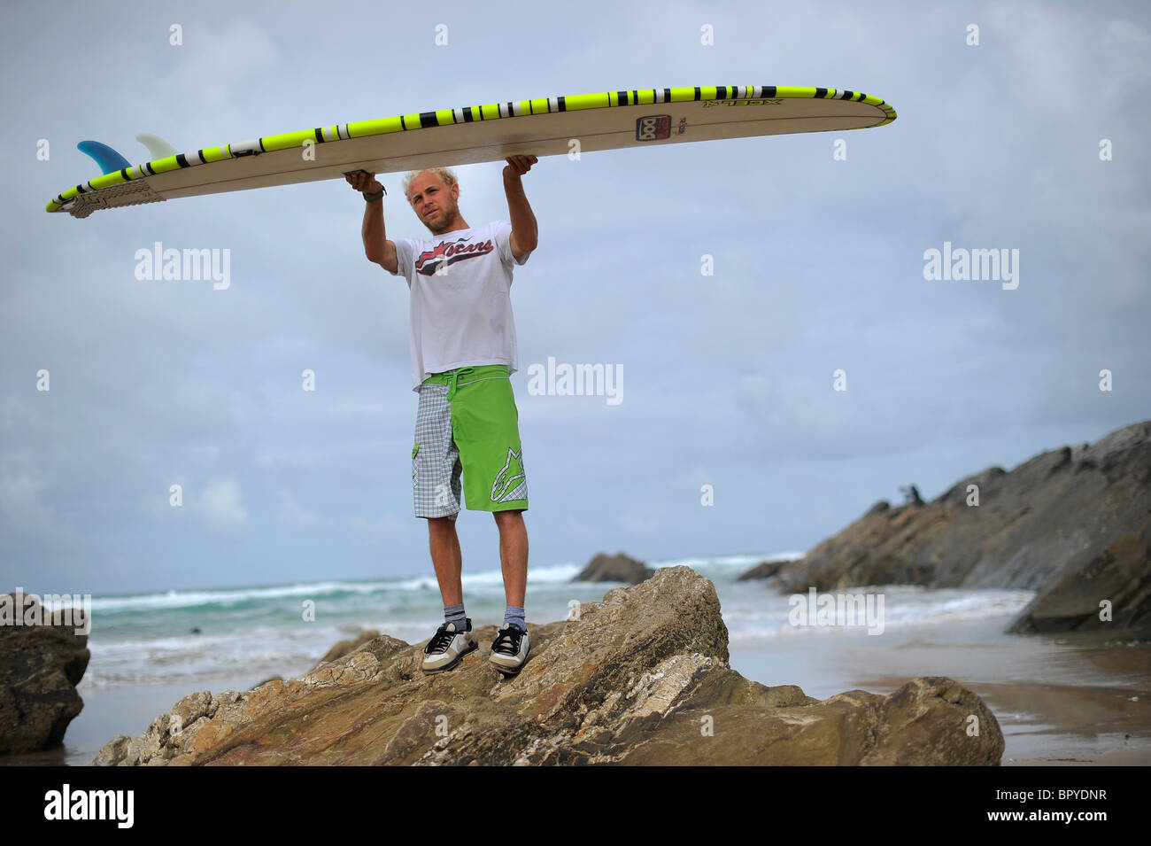 A surfer, Ben Howey, holding a longboard surfboard on the beach at