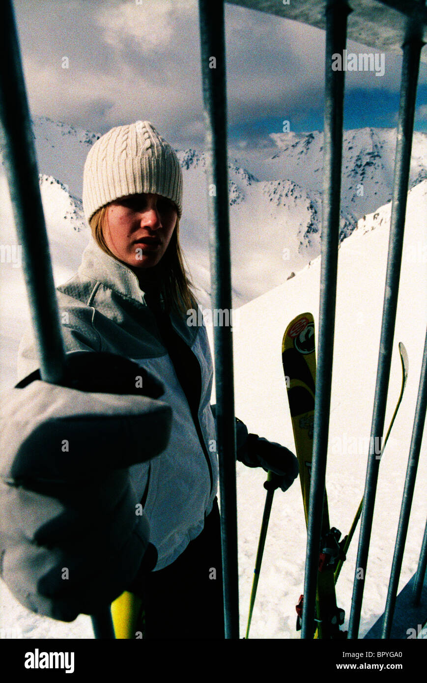 A woman stands behind a fence at a ski resort. Stock Photo