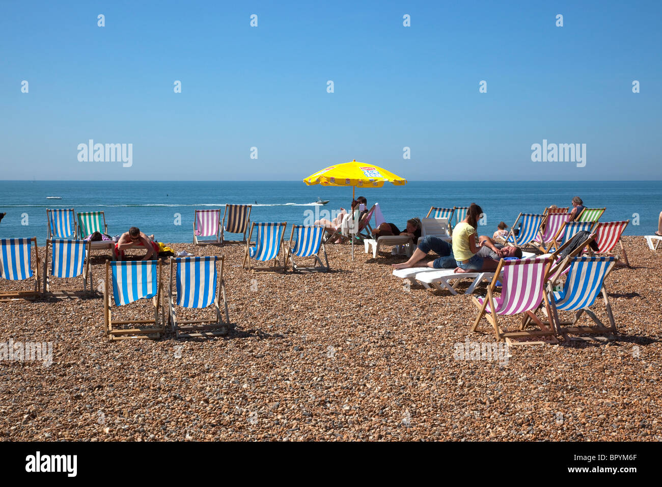 England, East Sussex, Brighton, Deck chairs and sunbathers on the pebble beach. Stock Photo