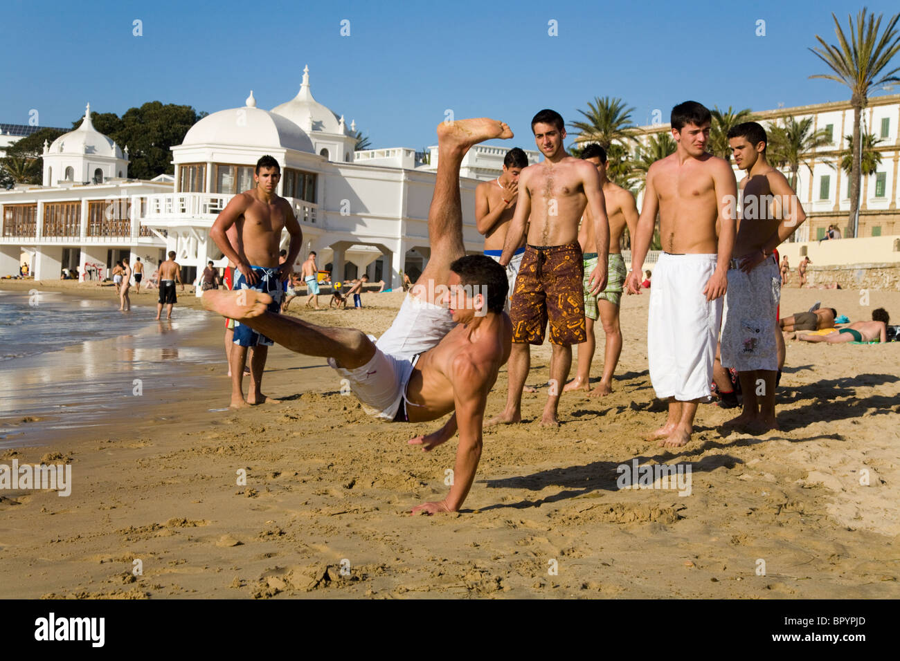 Spanish teenage boy / man practising/ practises his exercise & acrobatic skills in front of friends on a beach at Cadiz. Spain. Stock Photo