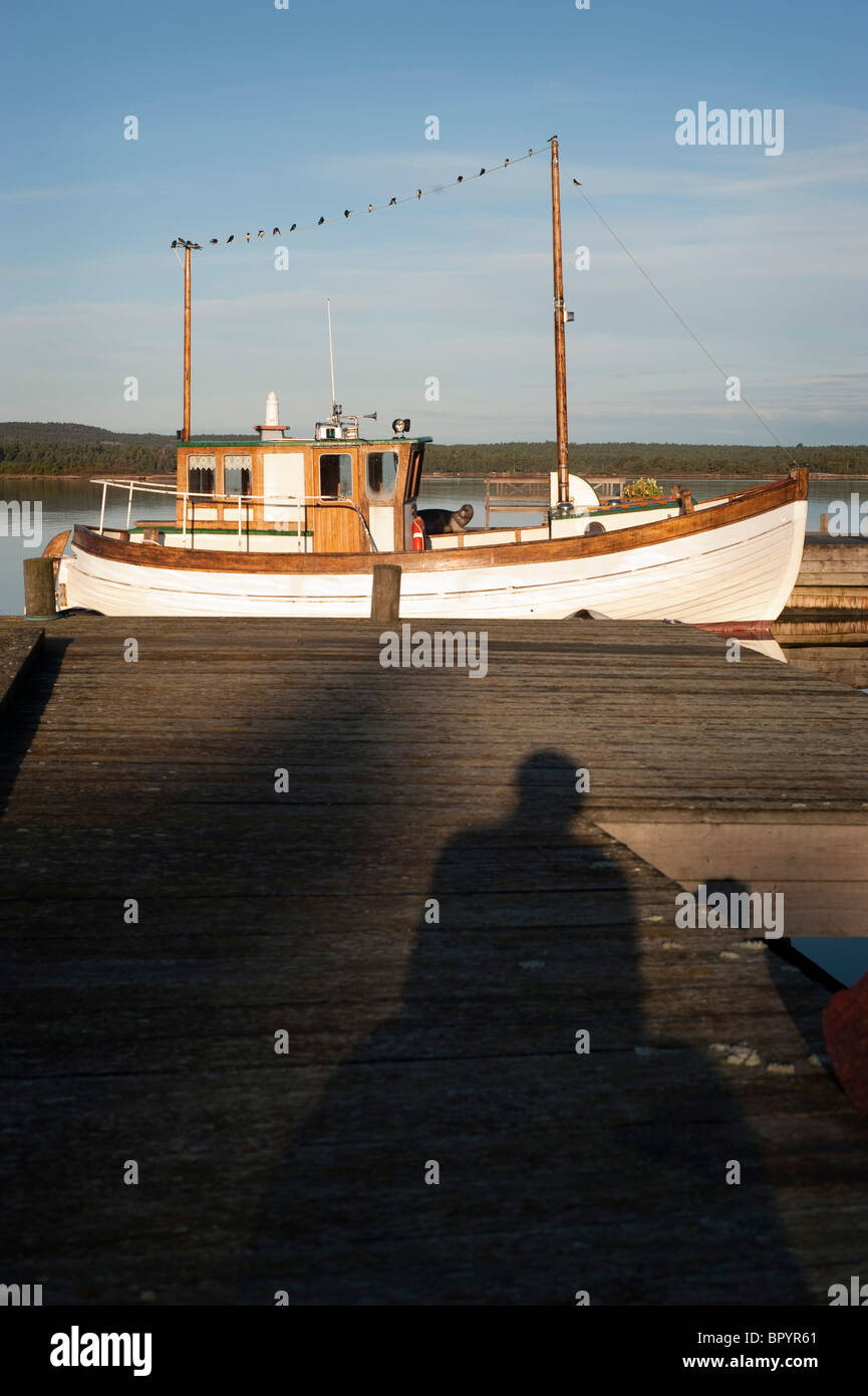 Fishingboat by bridge at sunrise, birds on boats wire, shadow of person in foreground Stock Photo