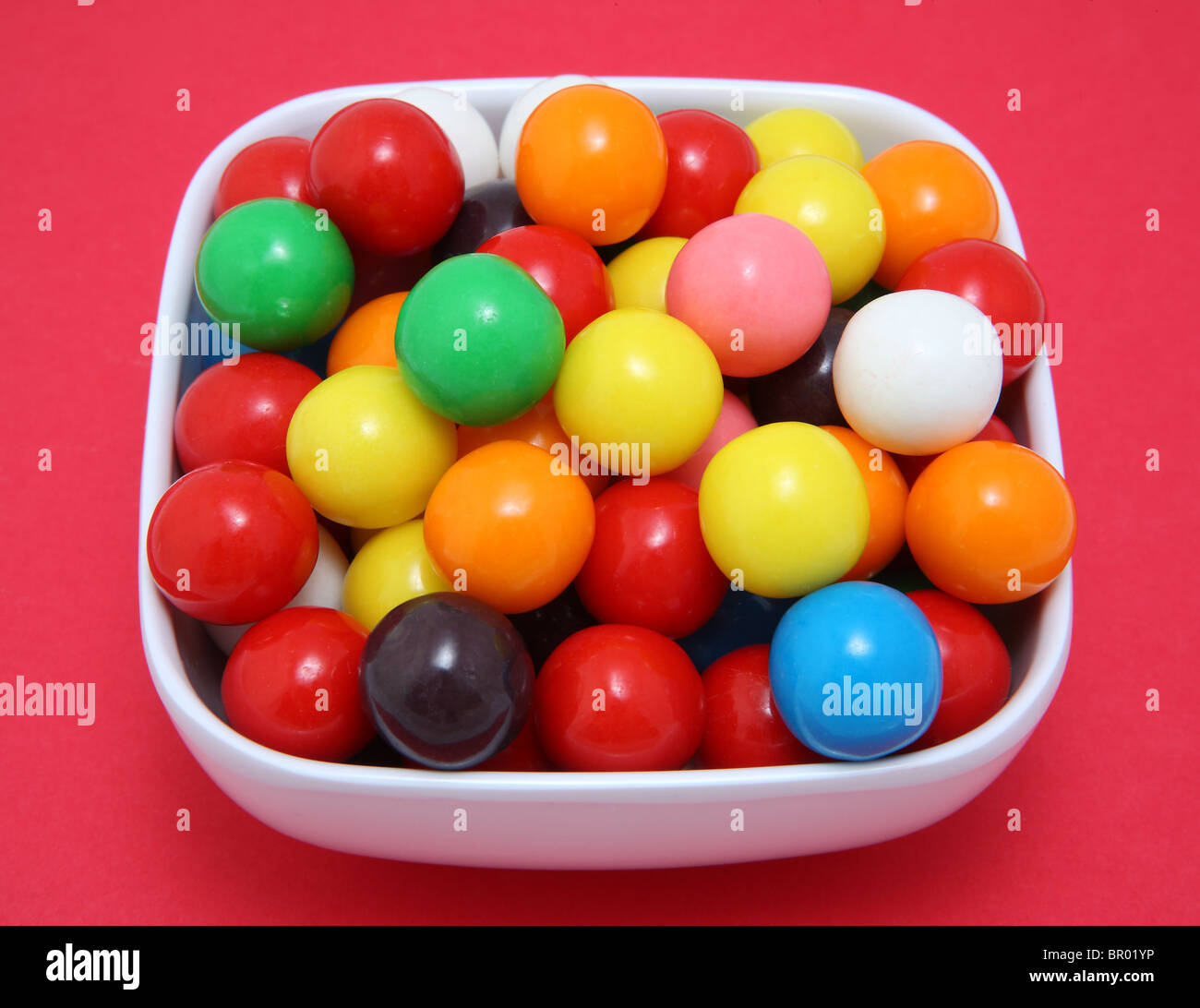 Colorful gumball candy in white bowl on red surface Stock Photo