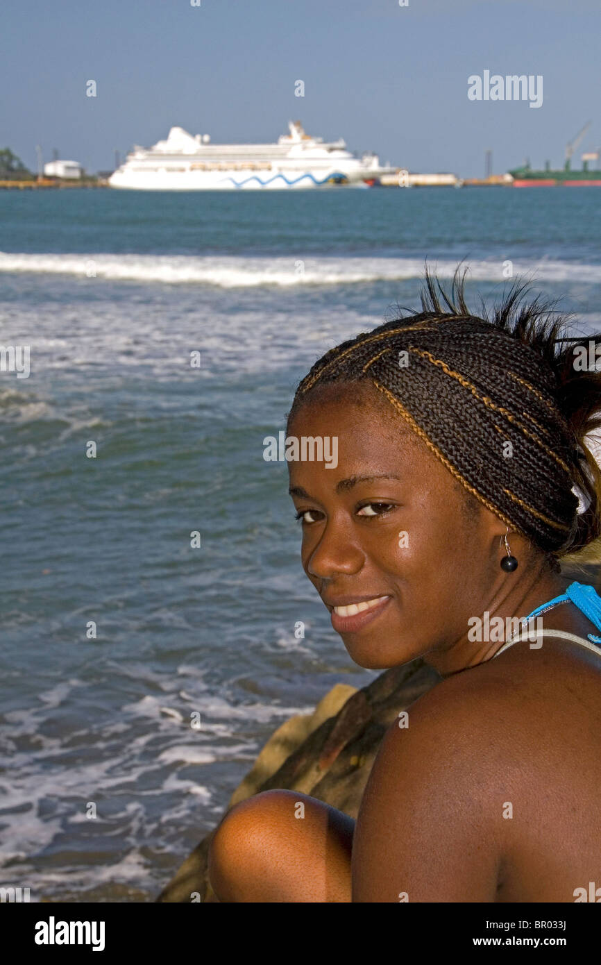 Costa Rican afro-caribbean woman on the beach with the AIDAaura cruise ship docked in the background at Puerto Limon, Costa Rica Stock Photo