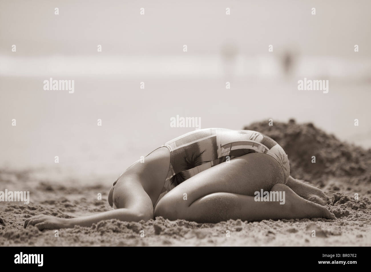 Girl on beach with her head buried in the sand Stock Photo