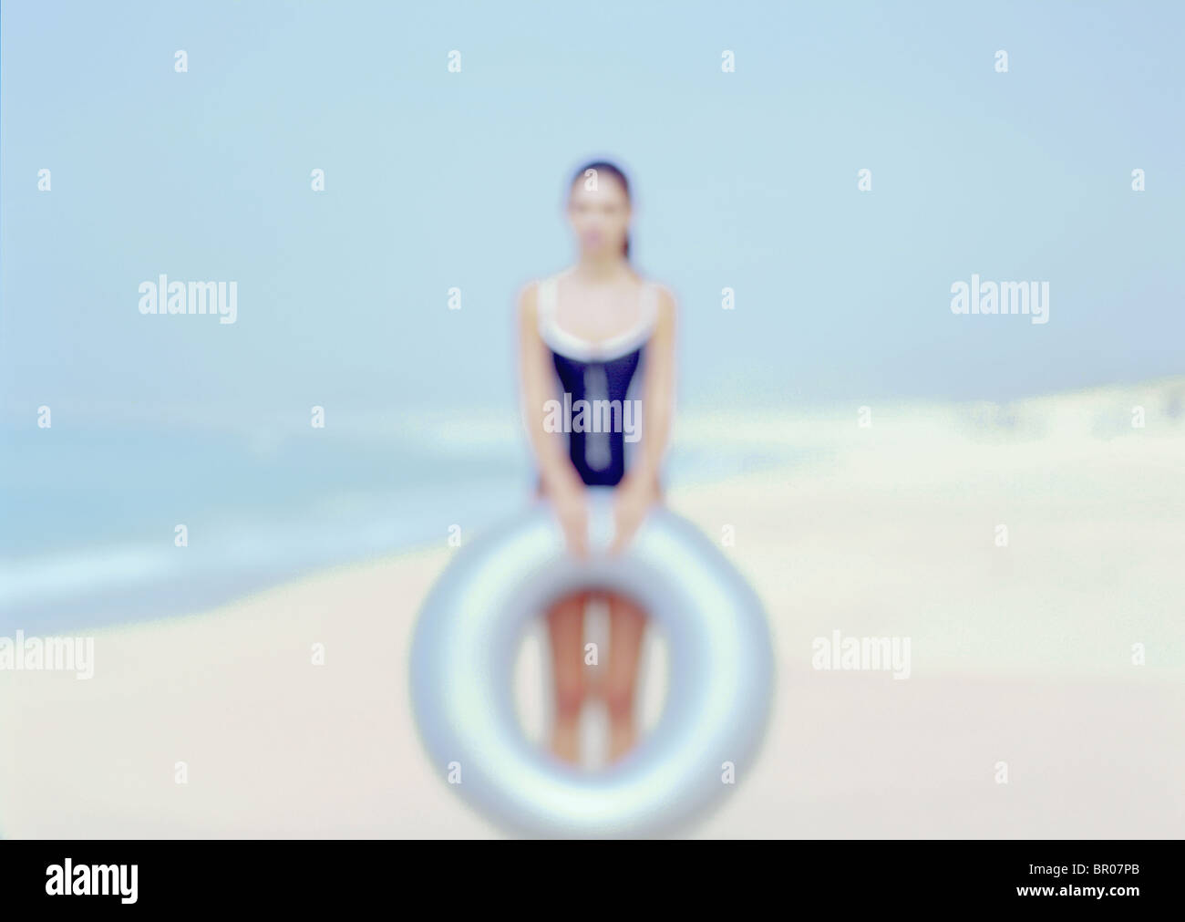 Out of focus causasian woman on a beach wearing a blue swimming suit and holding a light blue intertube. Stock Photo