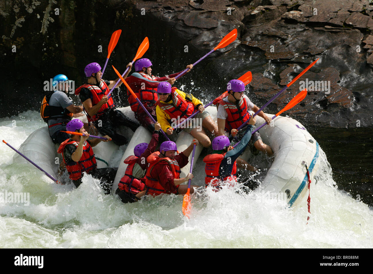 Whitewater rafters ride up onto the side of rocks. Stock Photo