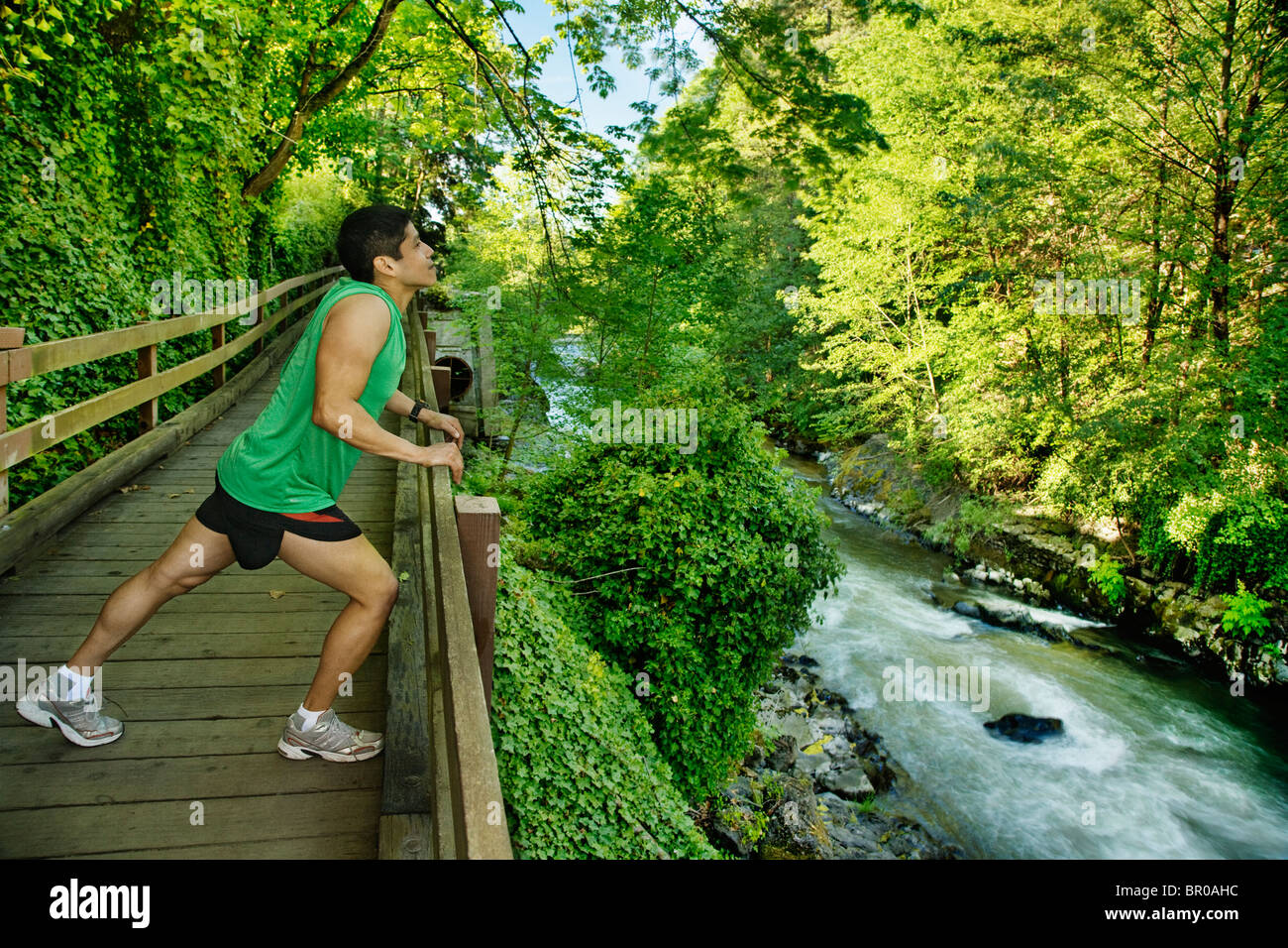 Mixed race runner stretching on walkway near river Stock Photo