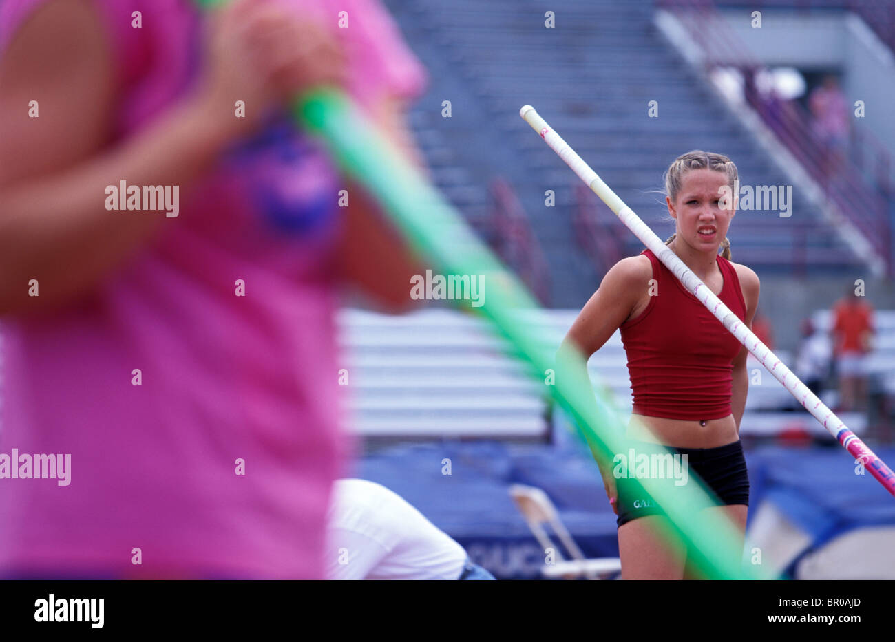 A teenage girl rests her pole on her shoulder in between pole vaulting jumps at a track meet. Stock Photo