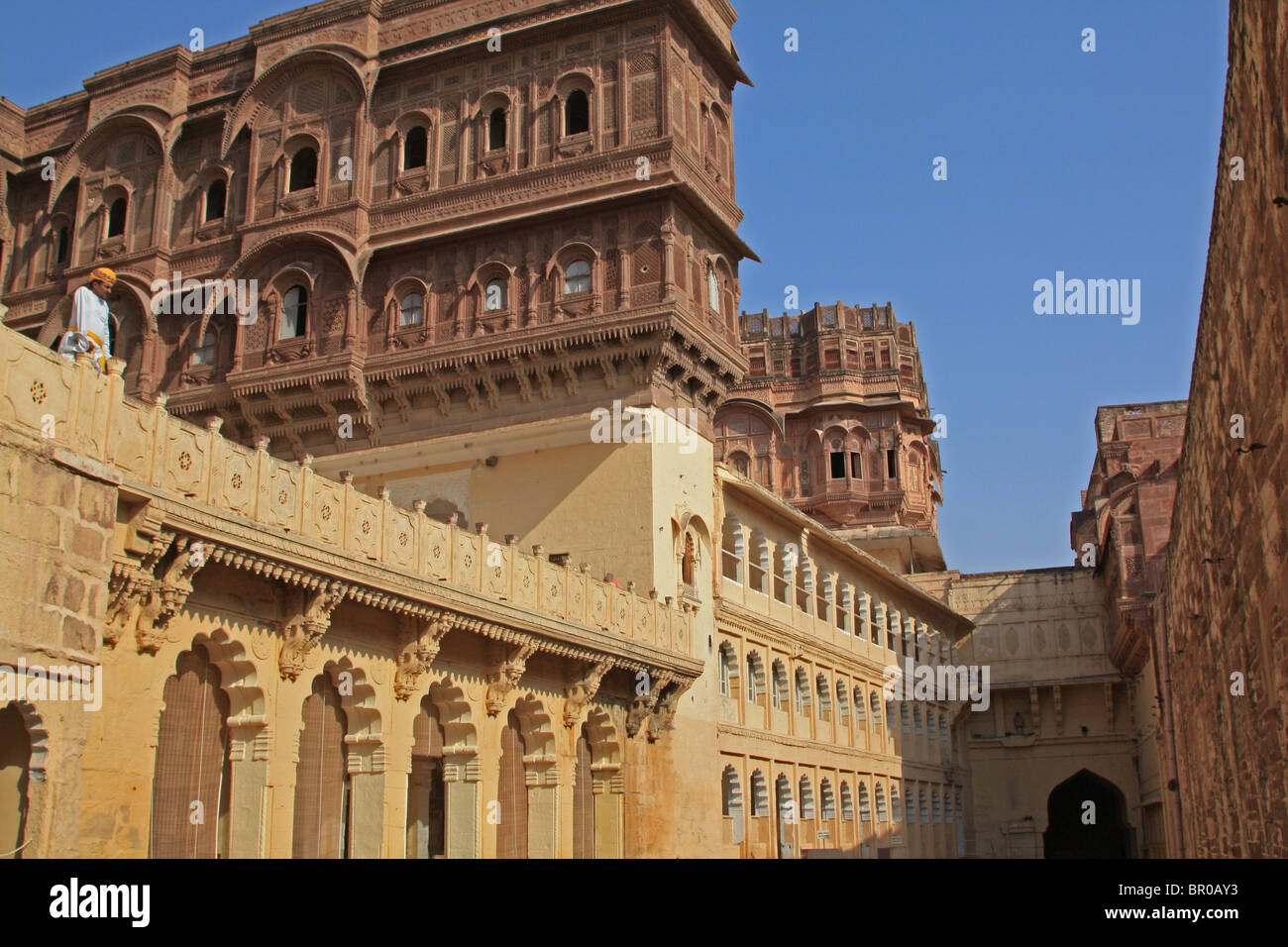 Turbaned guard under intricately carved orange and yellow  sandstone windows and parapets of Jodhpur  Mehrangar fortress Stock Photo
