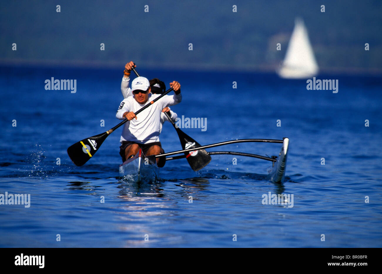 Two men paddling an outrigger on an alpine lake with a sailboat in the ...