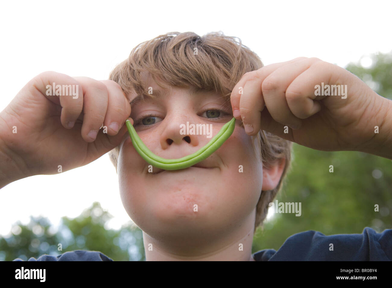 boy holding a green bean on his face pretending to have a moustache