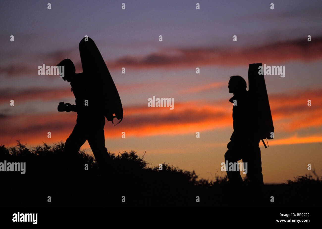 Two male rock climbers hike into a bouldering area at sunrise with their crash pads. Stock Photo