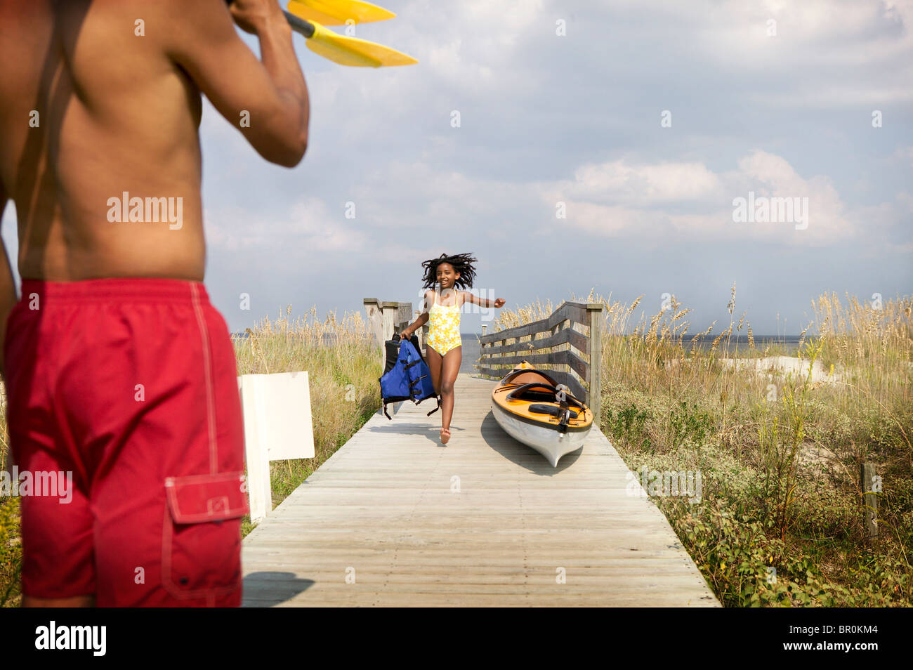 African American girl in swim suit on Florida beach boardwalk with kayak and father Stock Photo
