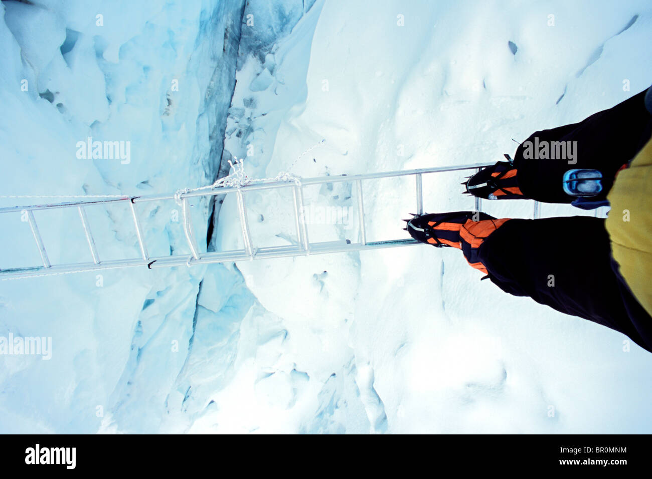 A climber on Mount Everest crossing a crevasse on a ladder in the Khumbu icefall in Nepal. Stock Photo