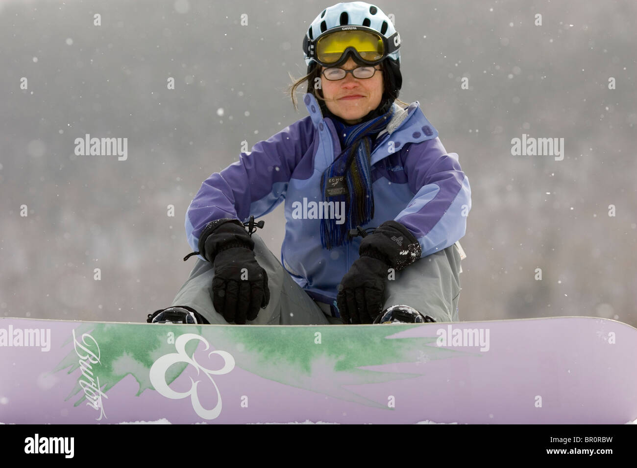 A young woman smiles with her snowboard while on vacation at Sunday River ski resort in Bethel, Maine. Stock Photo