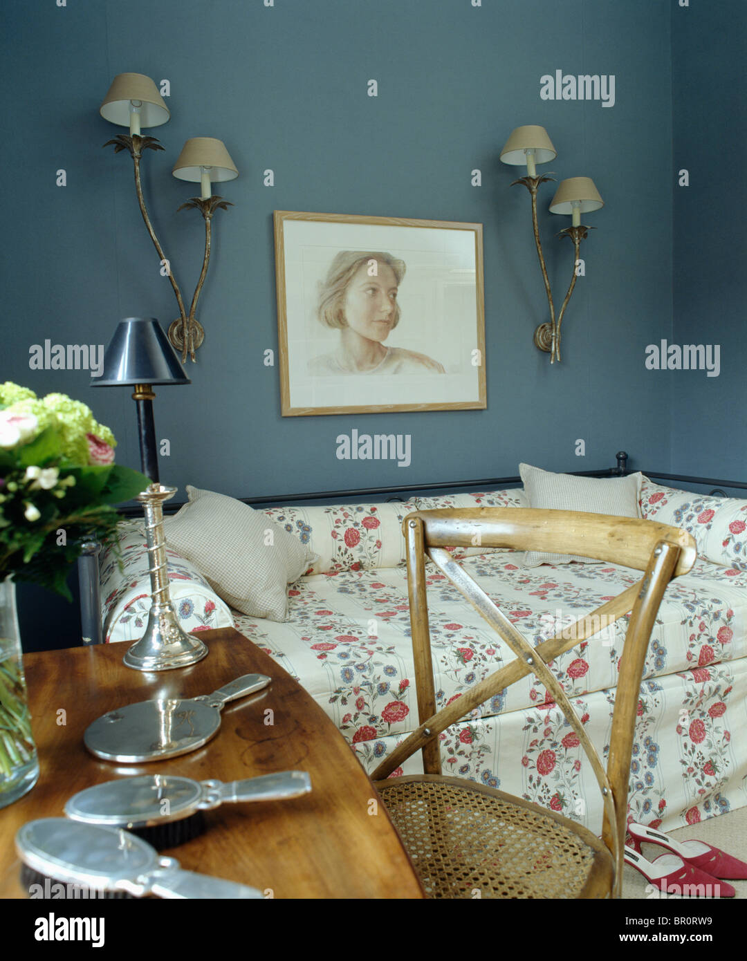 Picture on wall above sofa-bed with floral bed-cover in dark blue study  bedroom with silver dressing-table set on antique table Stock Photo - Alamy