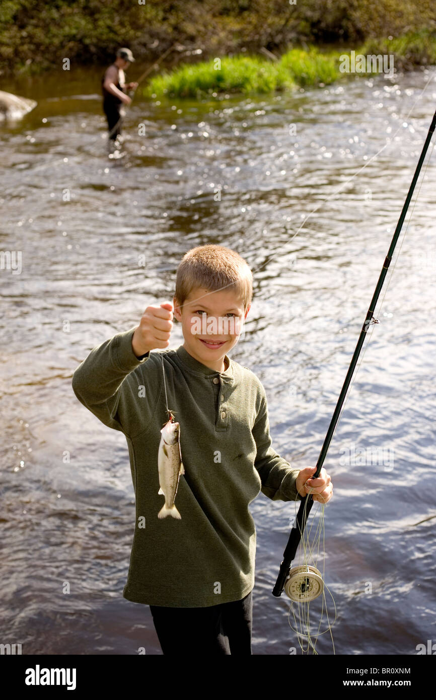 A young boy holds up a fish he caught while fly fishing on the Moose