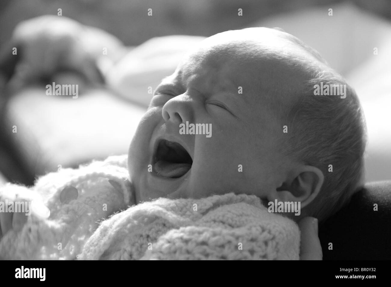 7 week old baby crying in the arms of her mother Stock Photo