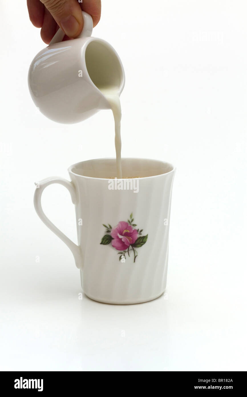 Pouring milk into a hot drink in a white porcelain china mug on a white background Stock Photo