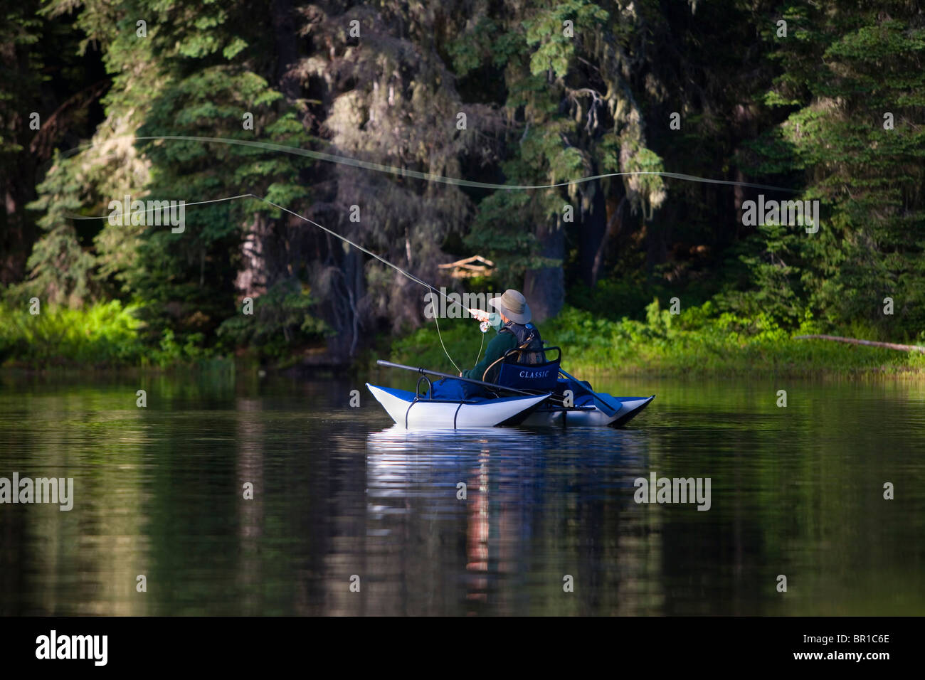 A flyfisherman casts from a pontoon boat on a lake in the Cascades of Washington State. Stock Photo