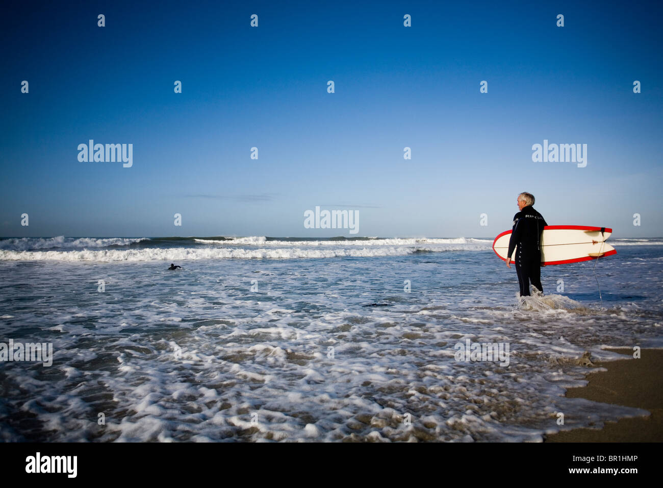A surfer stands at the waters edge and prepares for a session in Carlsbad, CA. Stock Photo