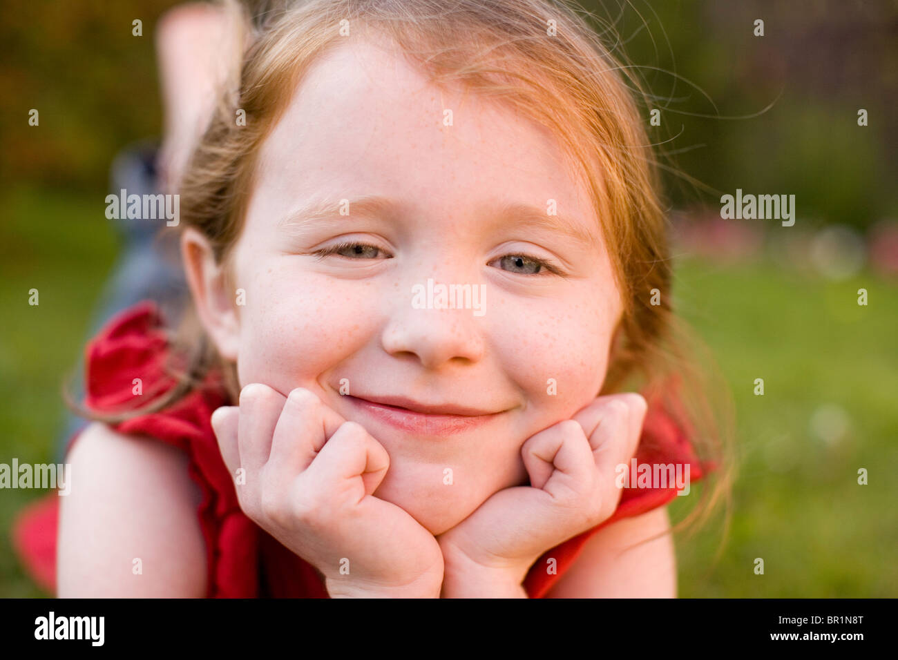 Small BlueEyed Girl in Red TShirt Lying on Green Grass Smiling as She
