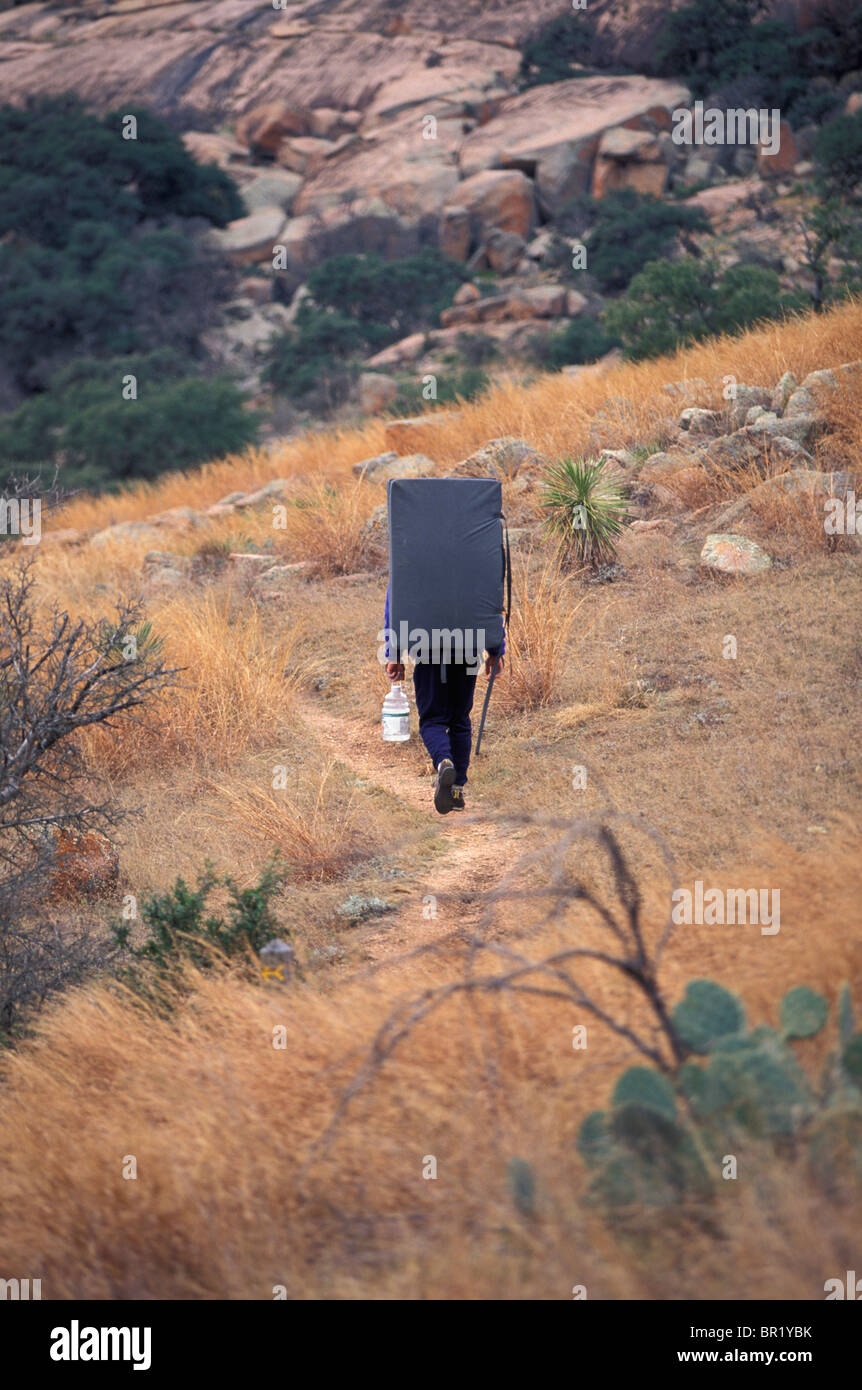 A climber hiking along a path with his crash pad near Austin, Texas