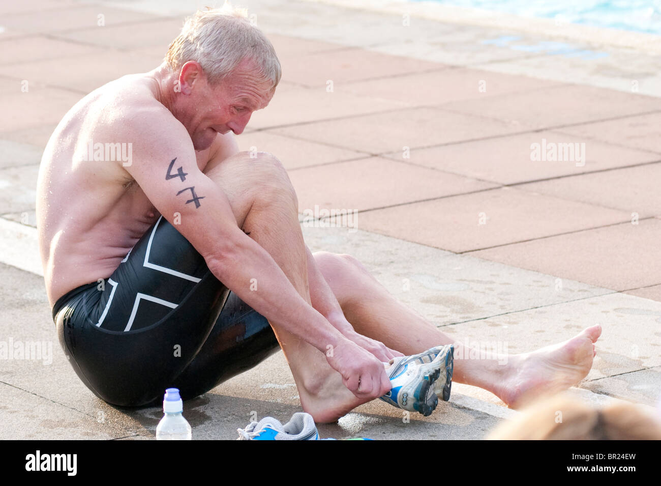A male triathlete struggles to get running shoes in the transition area after a 400M swim Stock Photo