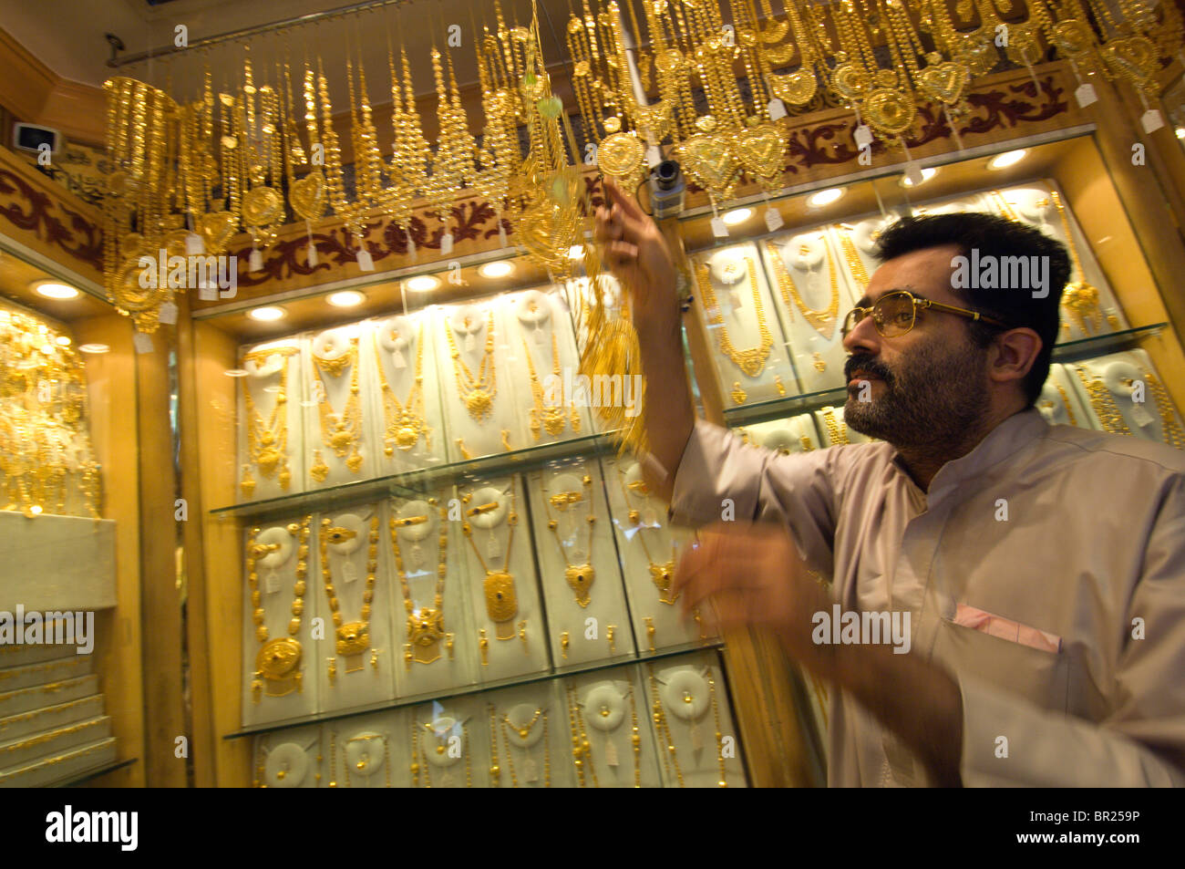 A shop keeper displays elaborate gold jewelry in the famous Gold Souk ...