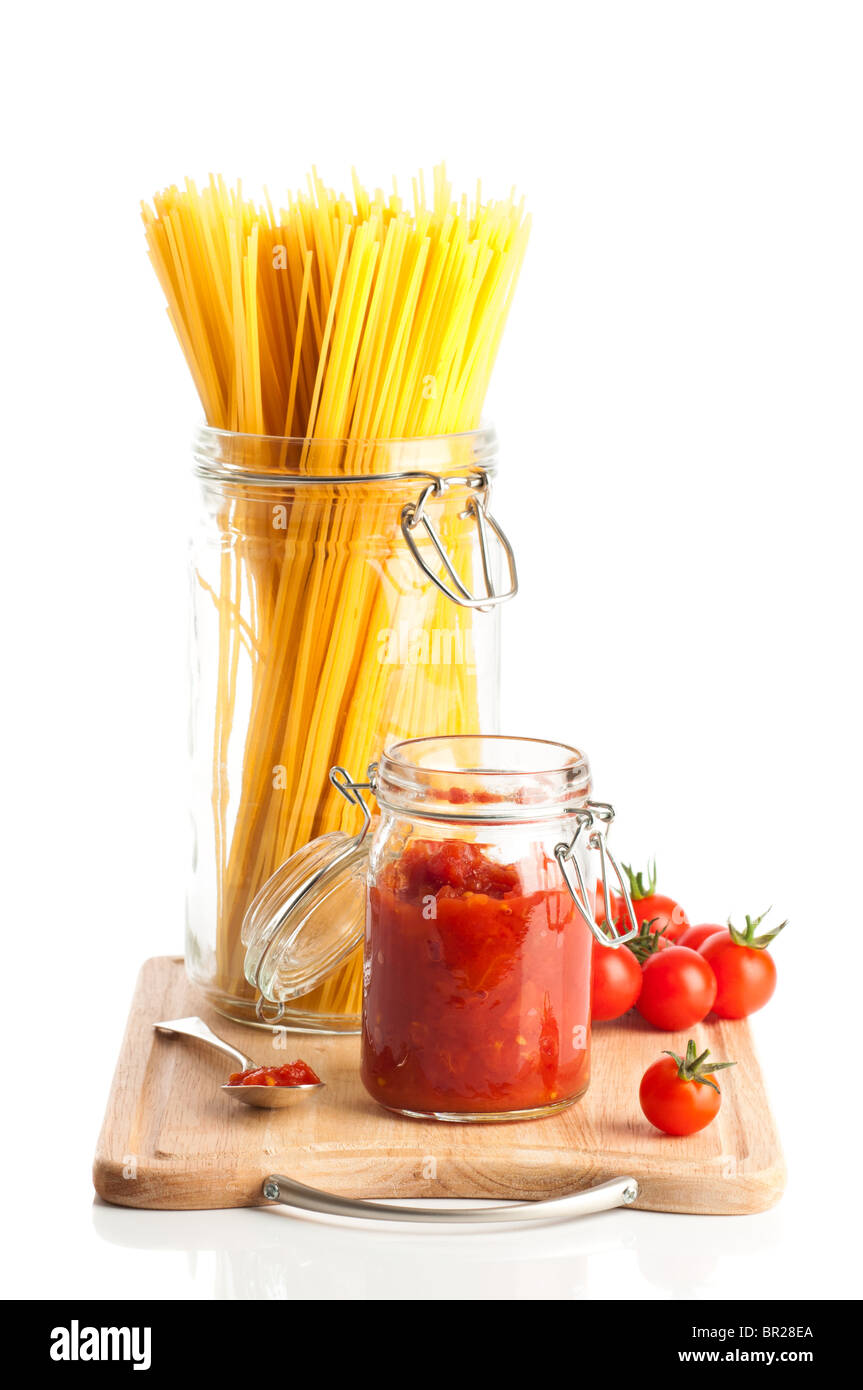 Tomatoes and spaghetti pasta in glass jars on wooden chopping board on white background Stock Photo