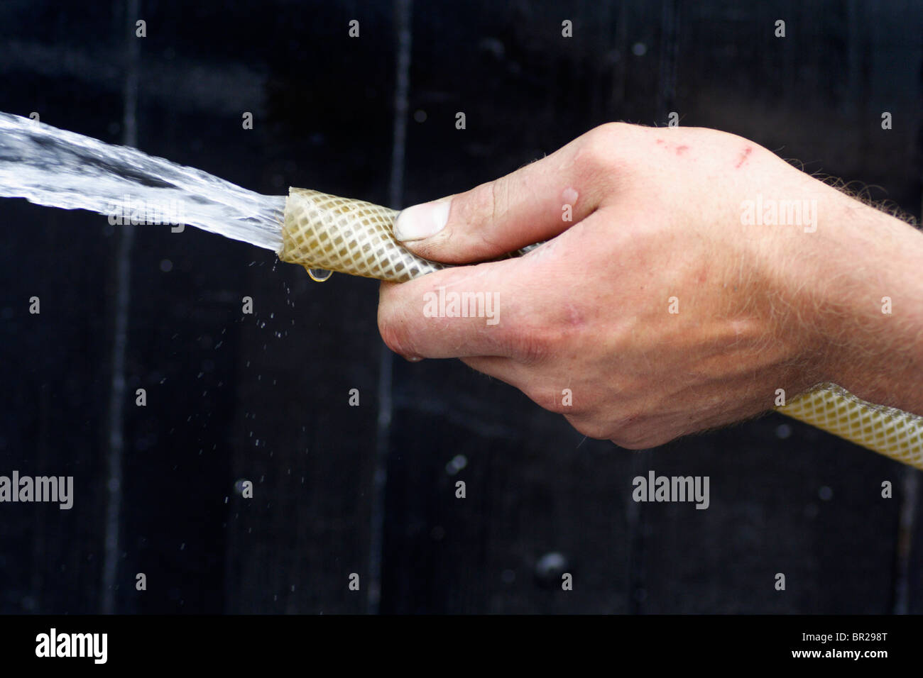 Hose pipe with water coming out held in a man's left hand Stock Photo