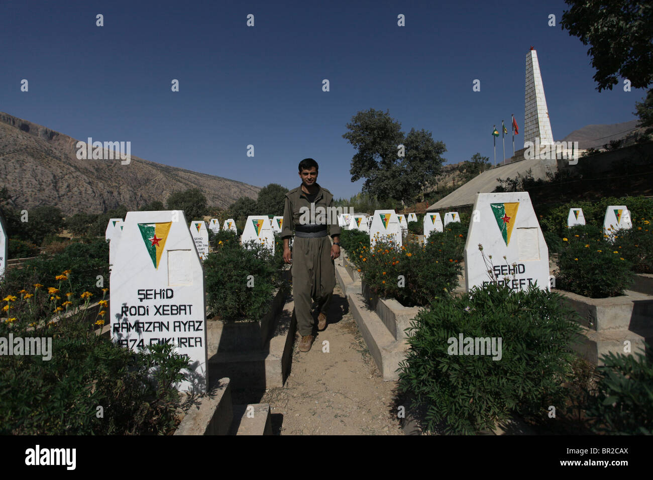A HPG Kurdish fighter amid tombstones in Mehmet Karasungur Cemetery which is burial site for fallen Kurdish fighters of the People's Defense Forces HPG the military wing of the Kurdistan Workers' Party PKK located in the Qandil Mountains a mountainous area of Iraqi Kurdistan near the Iraq Iran border Stock Photo