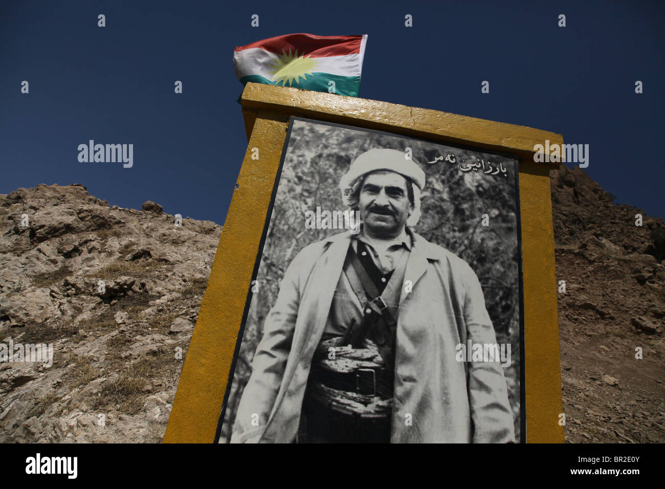 Kurdish flag waving over a roadside monument bearing the figure of historic leader Mustafa Barazani in Northern Iraq Stock Photo