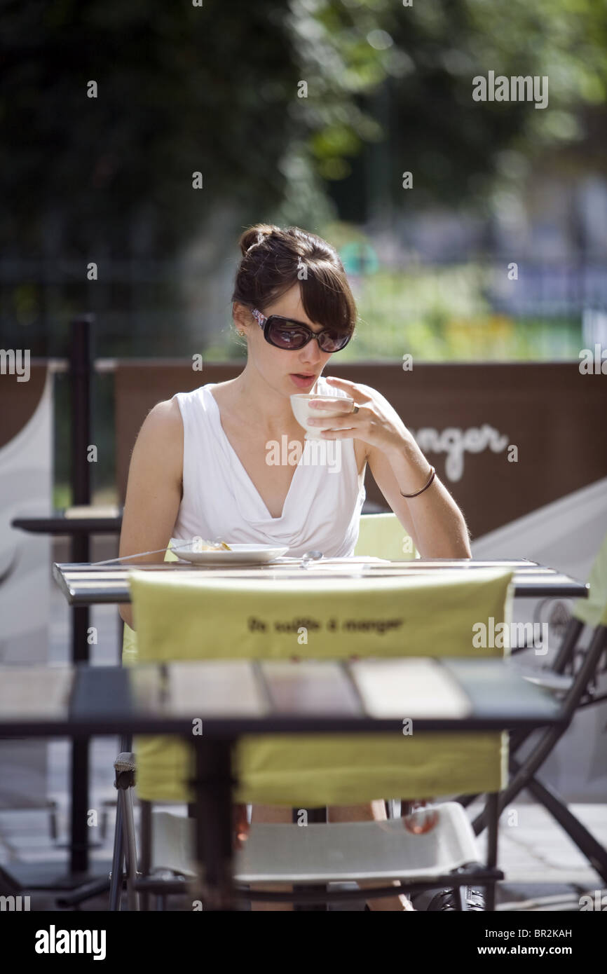 A young woman drinks coffee outside a cafe in the market on Rue Mouffetard, Paris Stock Photo